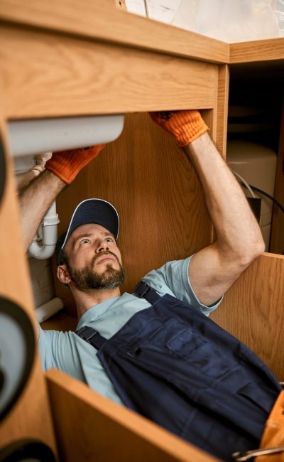 male-plumber-fixing-sink-pipe-in-kitchen-VNBHAW6